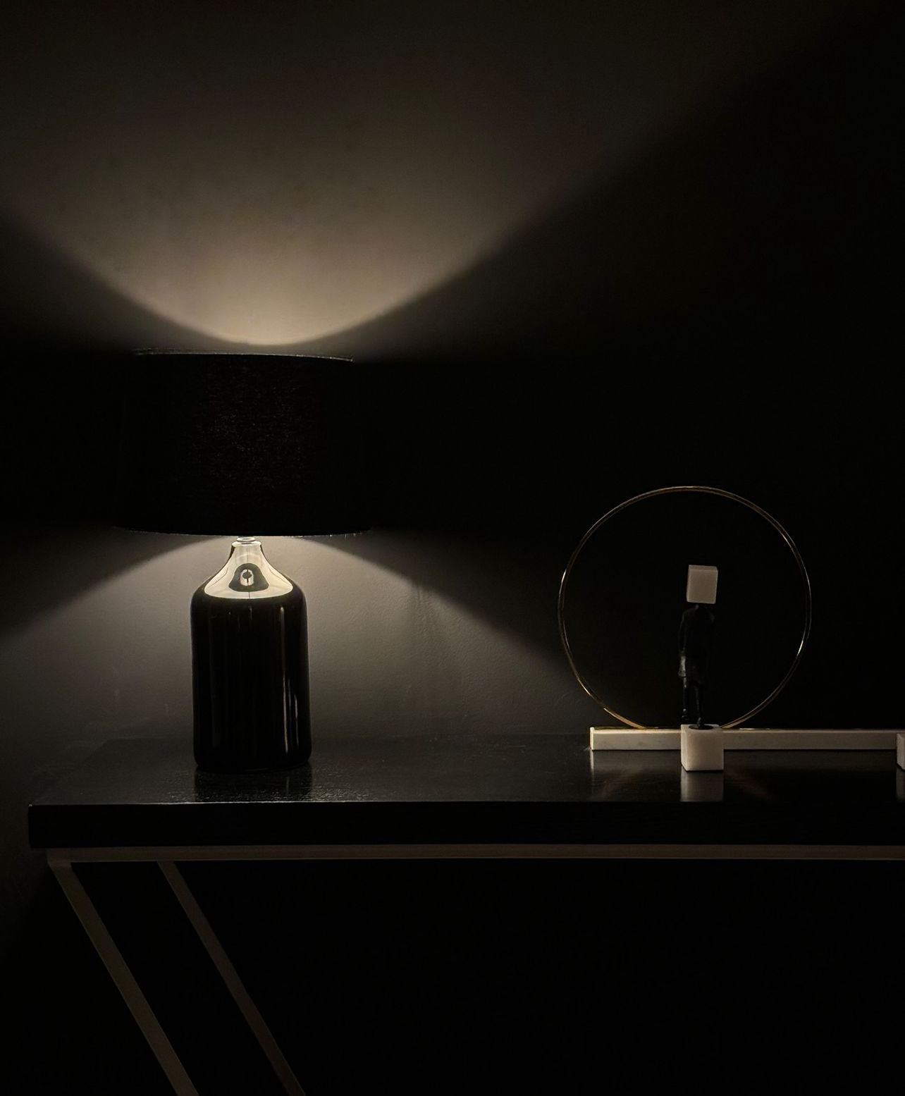 Console noire avec lampe en verre et sculpture circulaire dans la pénombre